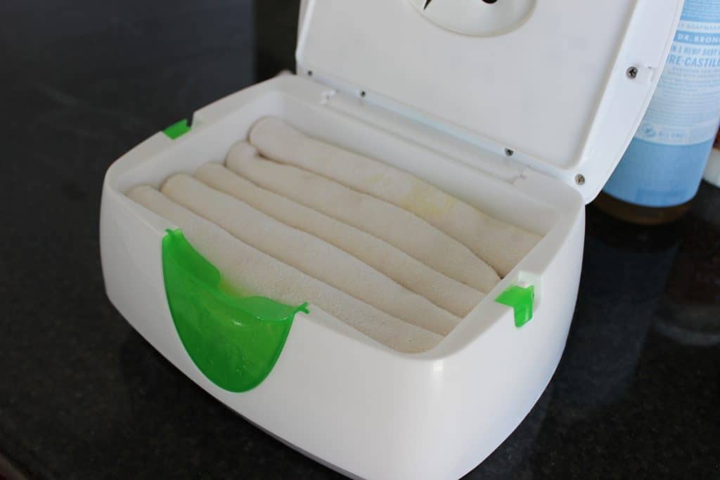 a row of five rolled up white cloth wipes in a wipe warmer