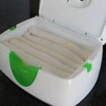 a row of five rolled up white cloth wipes in a wipe warmer