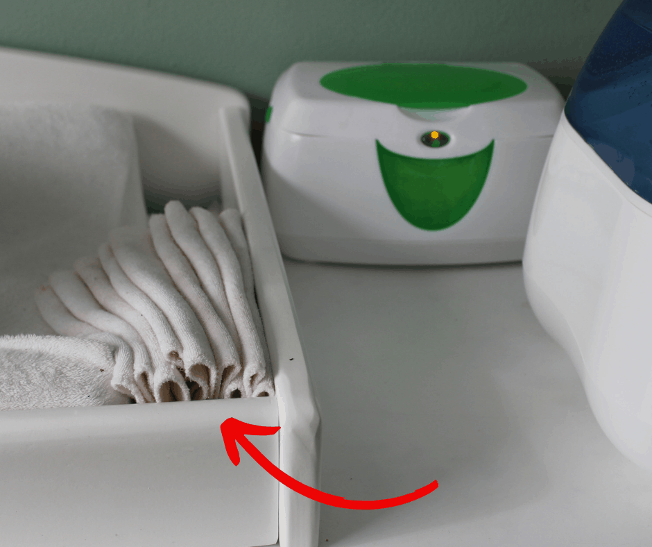 folded cloth wipes in between changing pad and dresser top with wipe warmer in the background