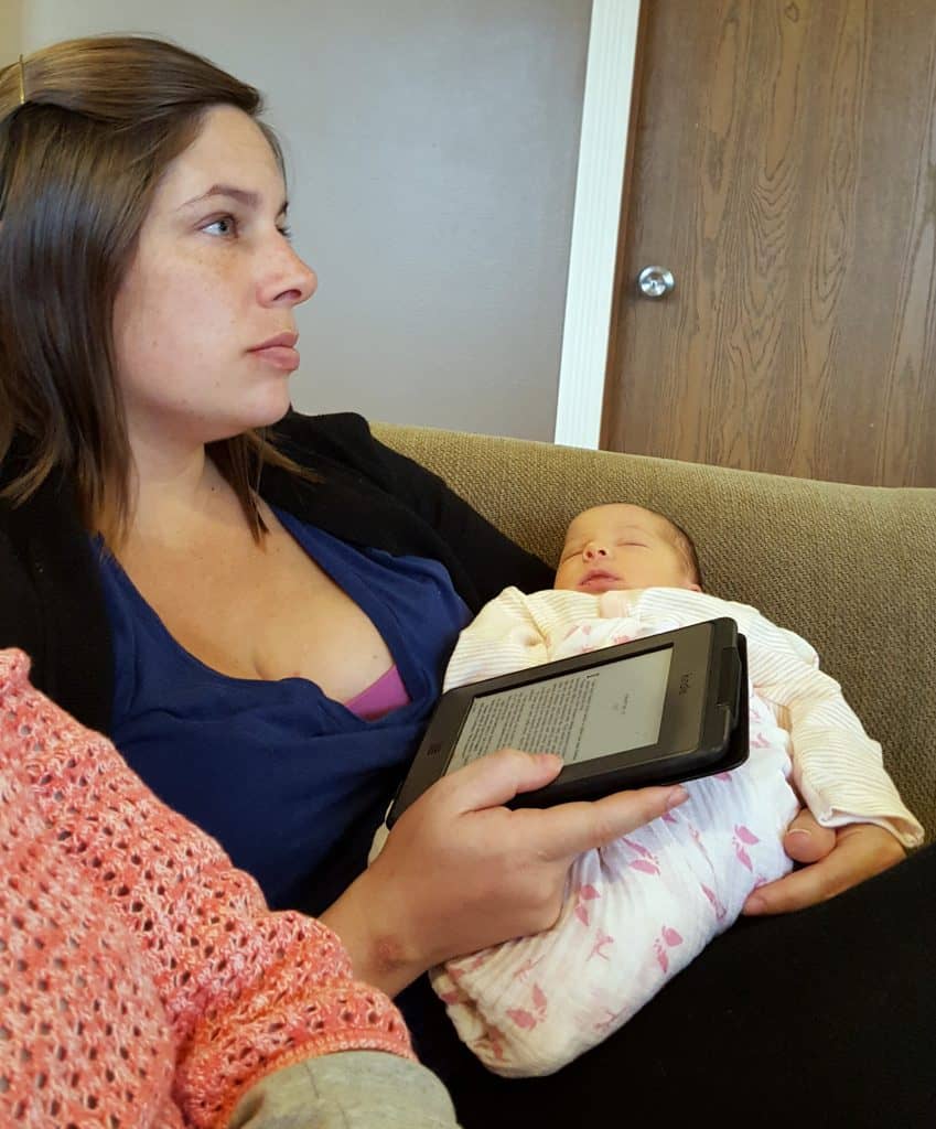 mom sitting down holding a Kindle and newborn