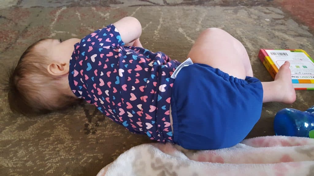 toddler laying on ground wearing blue cloth diaper