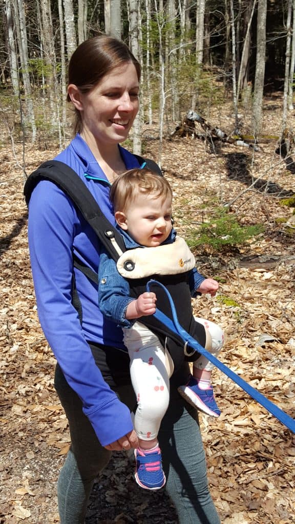 mom hiking with baby in front carrier holding a dog's leash