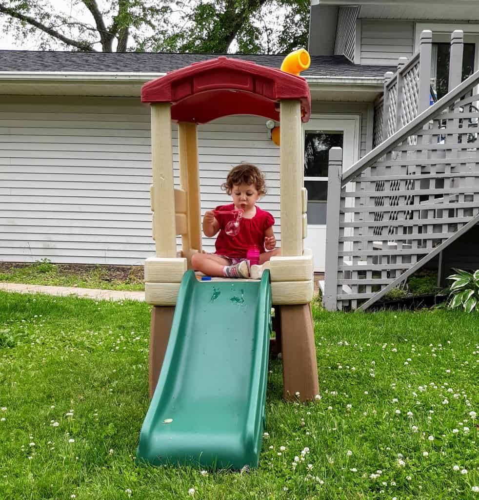 toddler blowing bubbles sitting in climber fort with slide