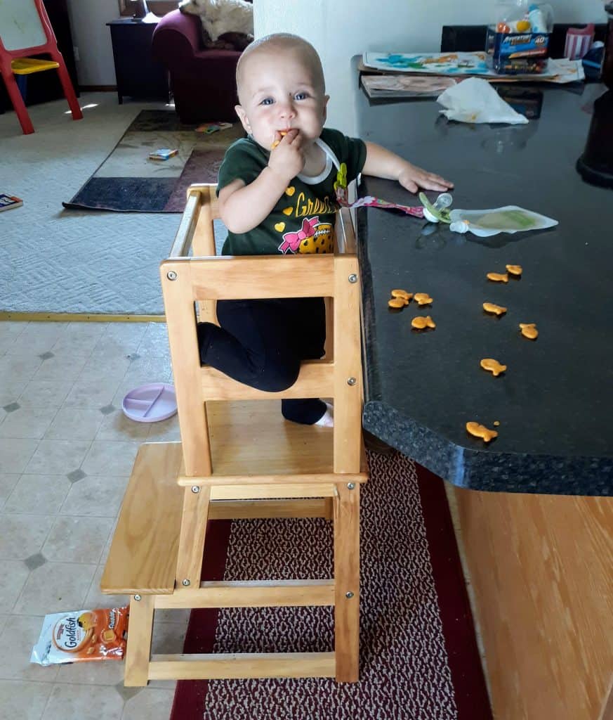 toddler standing on kitchen safety stool eating Goldfish