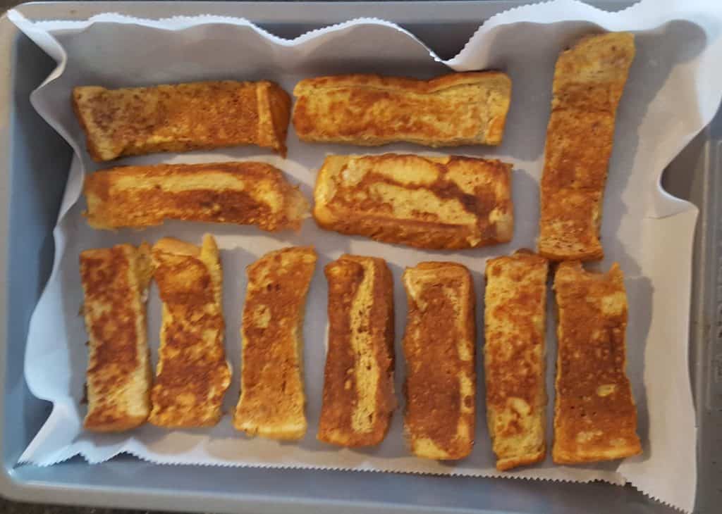 French Toast Sticks laid on top of parchment paper inside a 9x13 pan