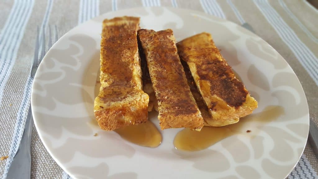 Three French toast sticks on a plate with syrup