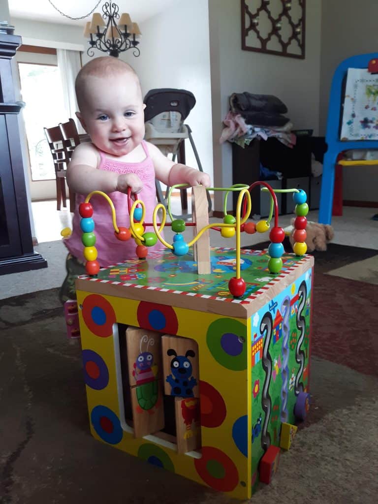baby standing holding on to wooden activity cube