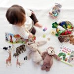 baby sitting surrounded by toys and books