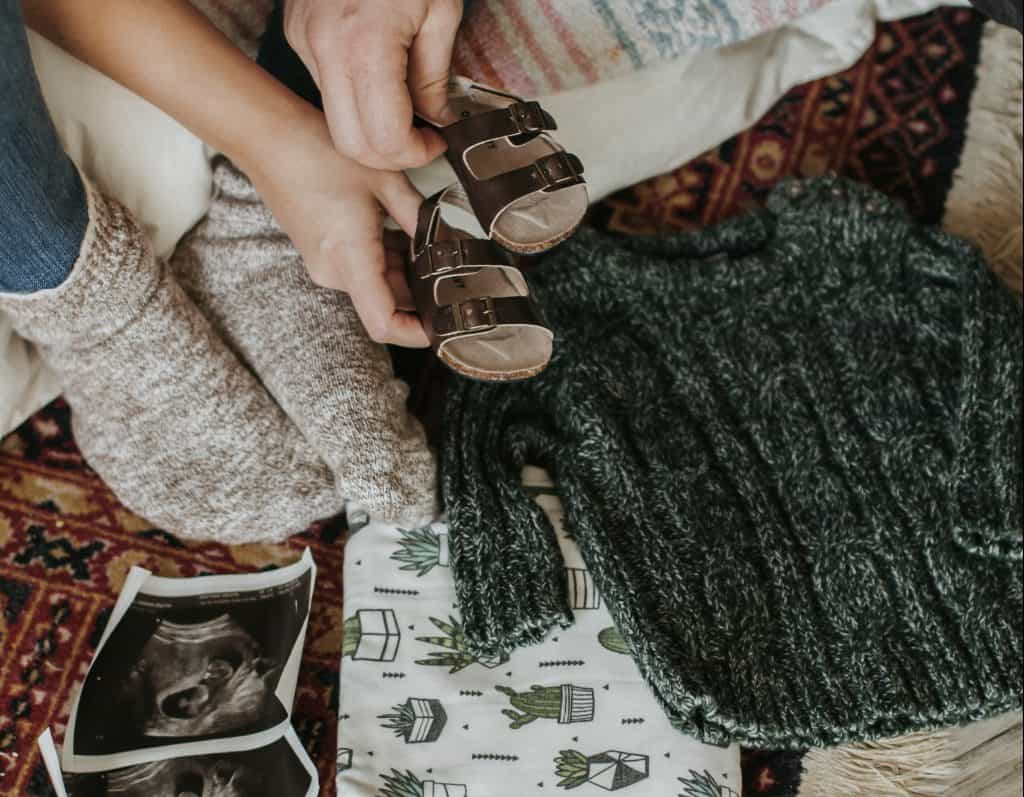 posed photo of ultrasound, gray baby sweater, and brown baby sandals