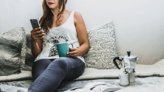 woman sitting on a bed with a cup of coffee and her cellphone