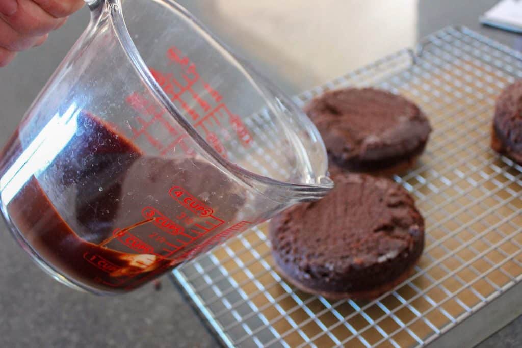 ganache in liquid measuring cup being poured over mini flourless chocolate cakes