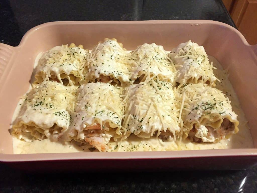 eight lasagna roll ups in a pan topped with alfredo sauce