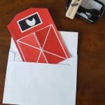 barn invitation sticking out of white envelope with an address stamper on the table