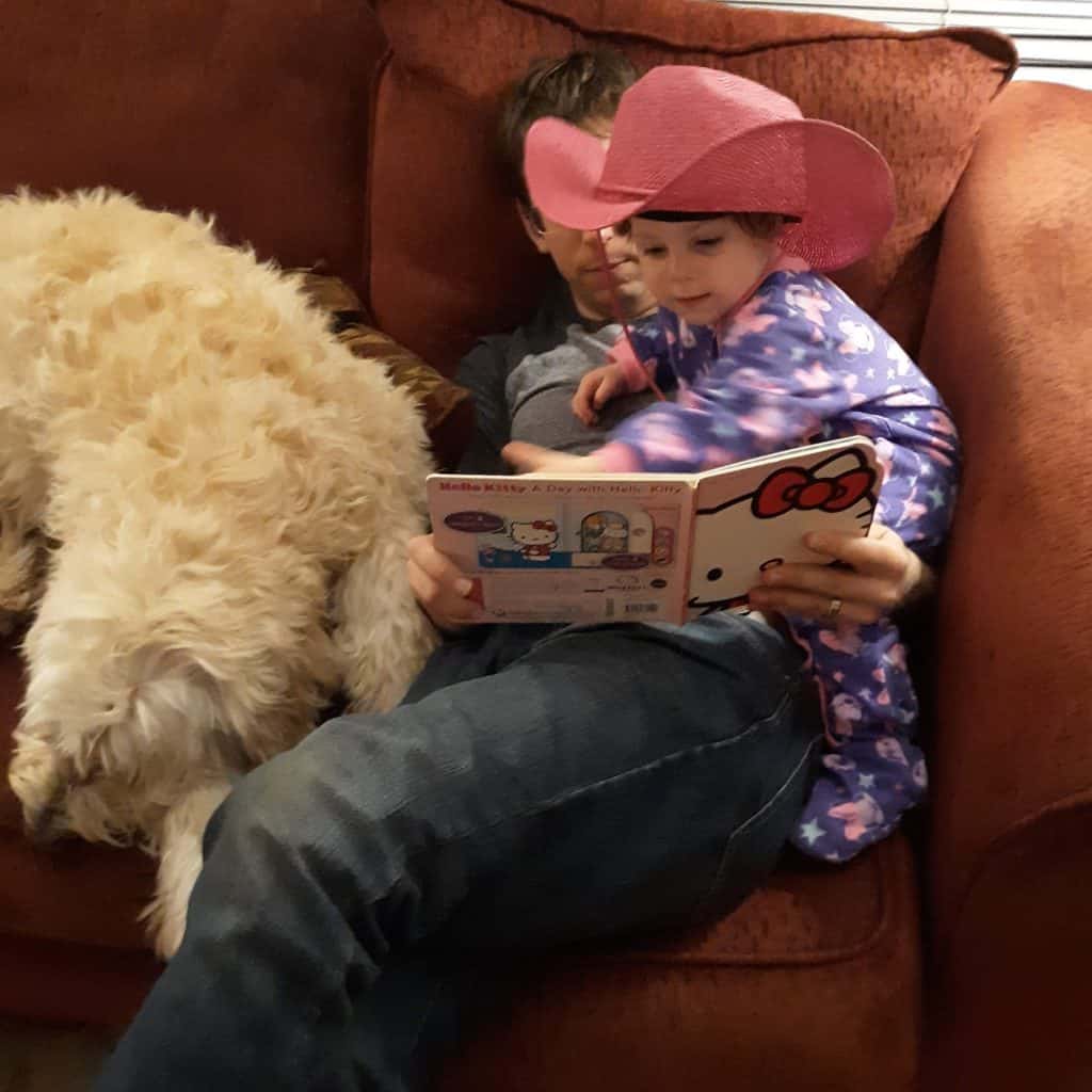 dad and toddler sitting on couch reading next to dog