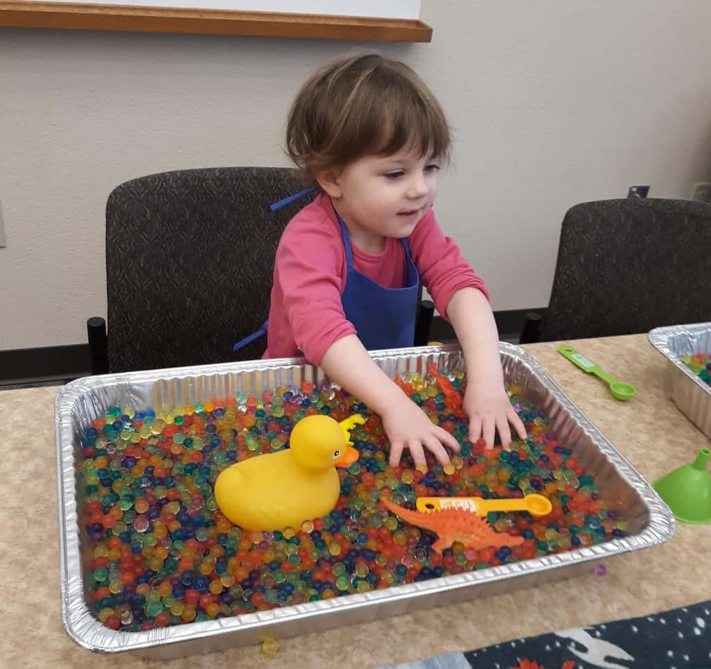 toddler playing in a large baking tin filled with water beads
