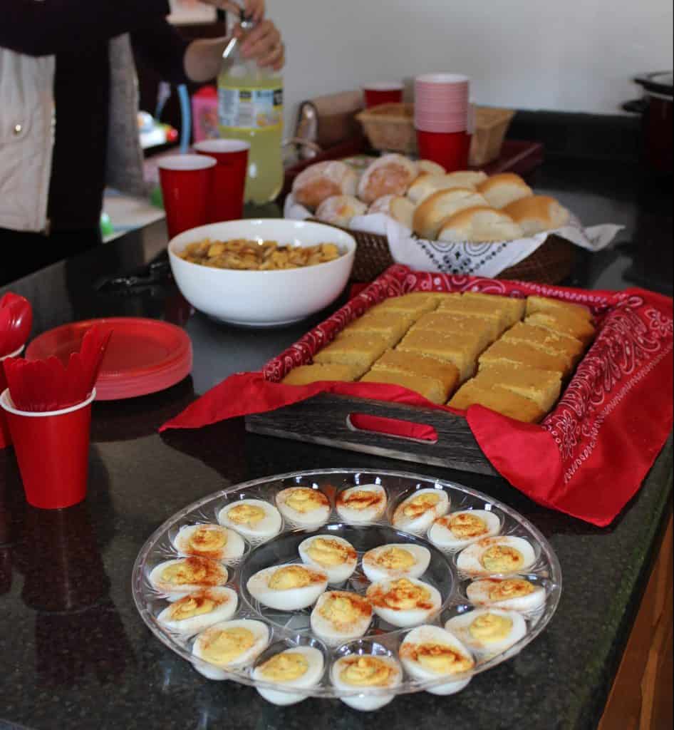 Tray of deviled eggs and a tray of cornbread.  A bowl of Chex Mix and a basket of rolls on a counter.