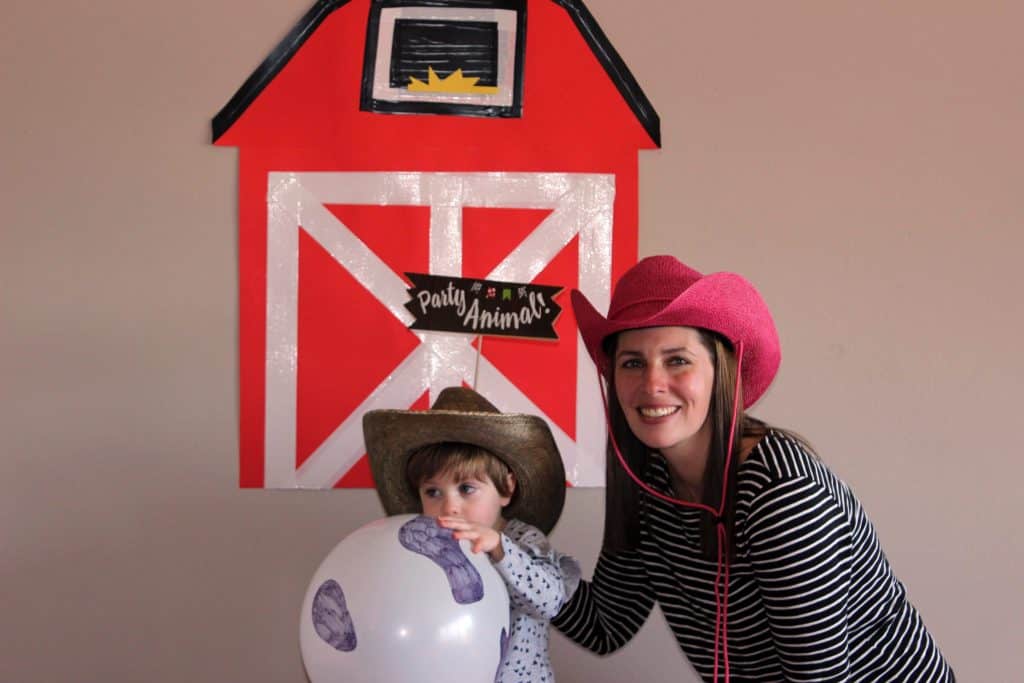 Mom and toddler posing in front of barn photo backdrop wearing cowboy hats