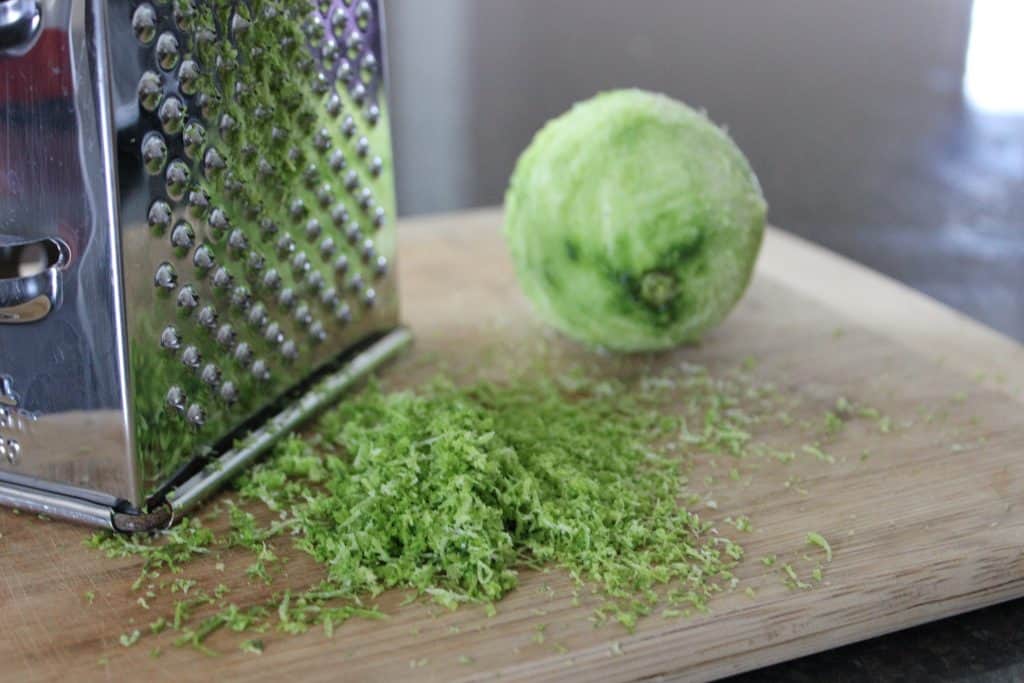 grater on a wooden cutting board with a pile of lime zest and a lime