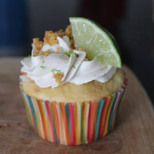 single cupcake on cutting board with whipped cream and lime triangle