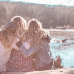 Three women sitting down outside with their arms around each other.