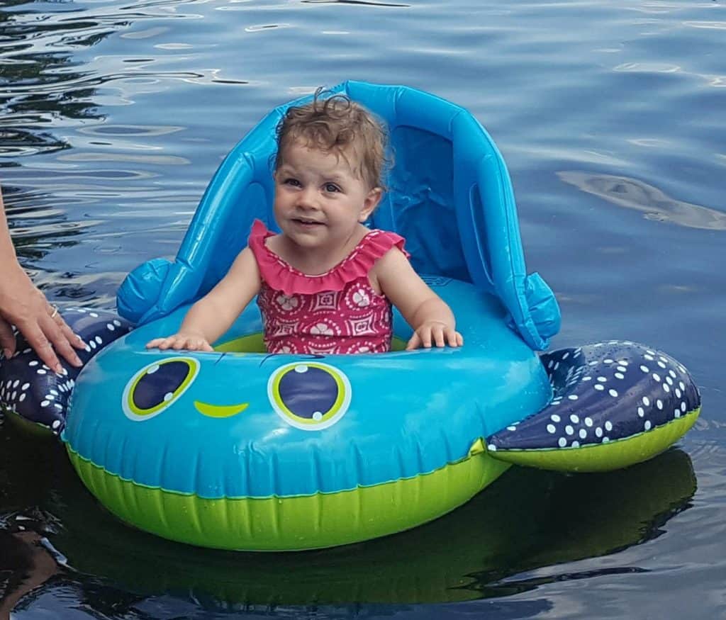 baby in pink swimsuit sitting in a baby float in the water