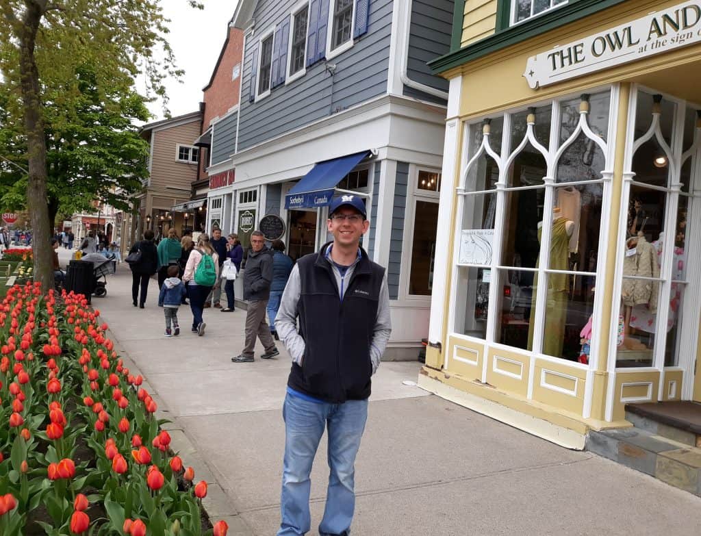 Husband standing on sidewalk in front of cute shops and next to tulips