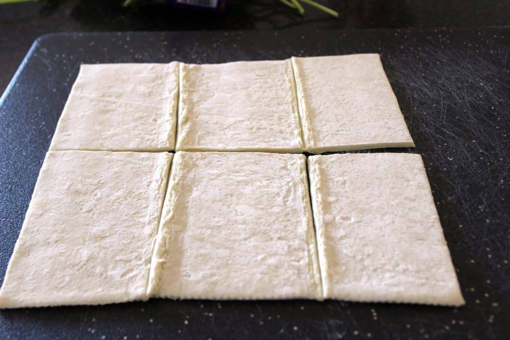 puff pastry sheet on a black cutting board sliced into six rectangles