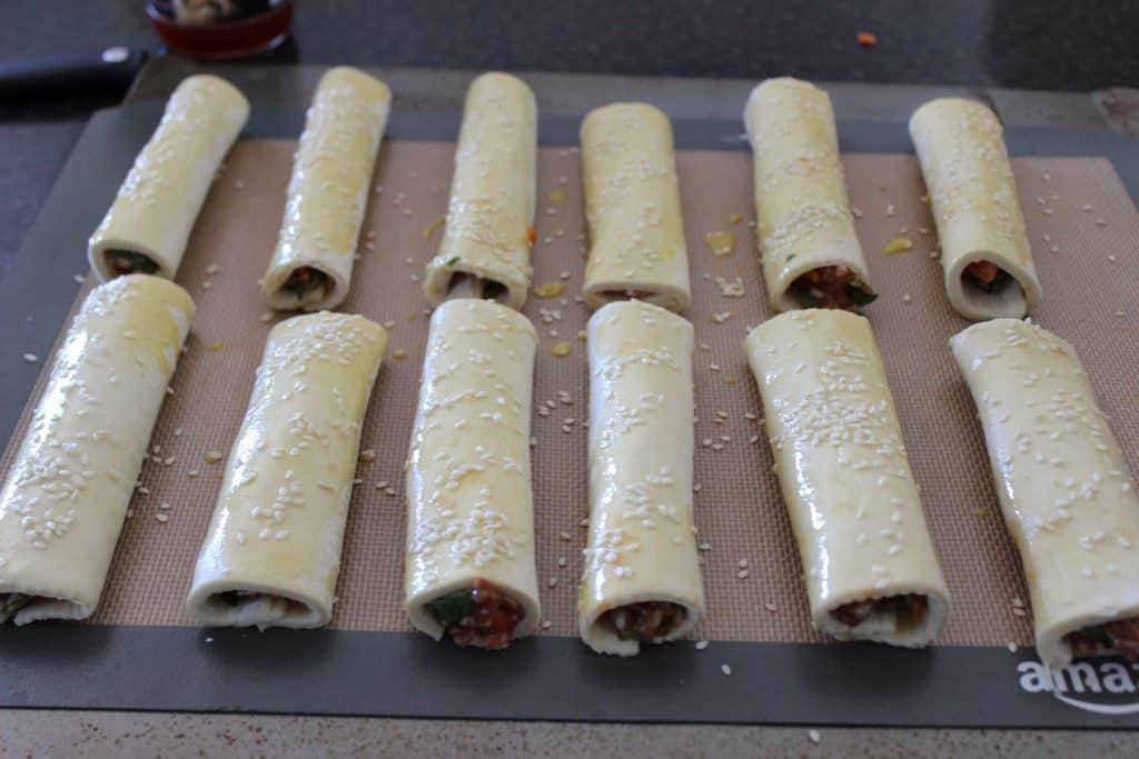 twelve unbaked sausage rolls on a silicone baking mat