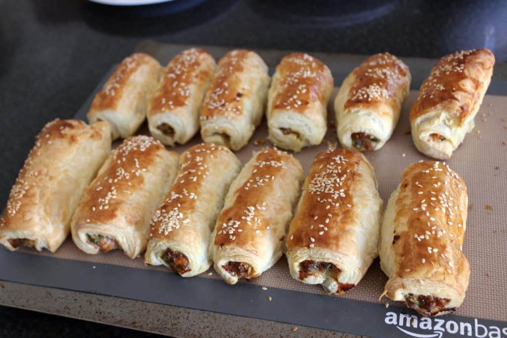 twelve baked sausage rolls on a silicone baking mat