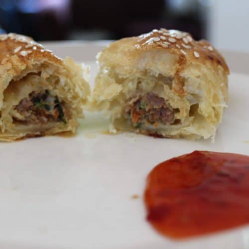 Baked Sausage Roll cut in half on a plate next to sweet chili dipping sauce