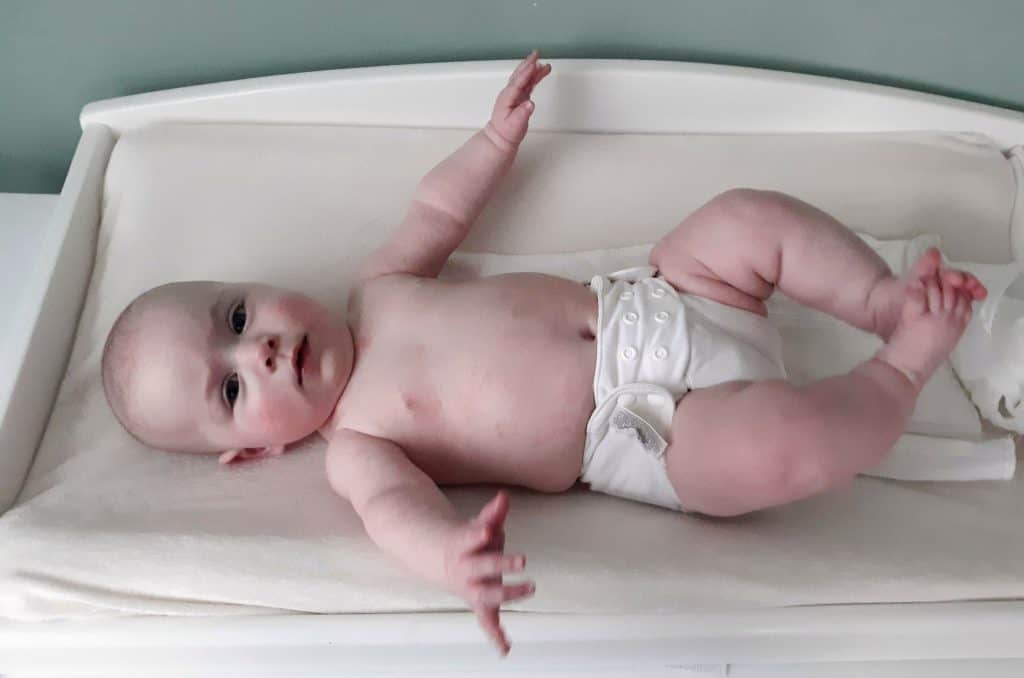 baby laying on changing mat in white cloth diaper