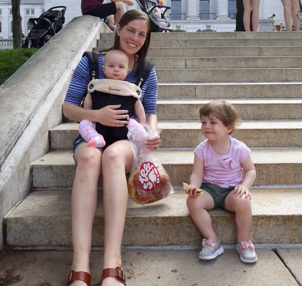 Mom carrying baby sitting on steps next to toddler eating bread