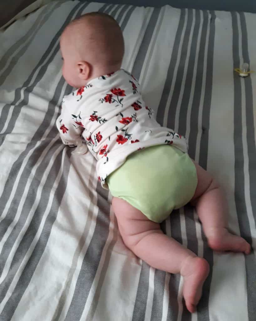 baby on tummy wearing a light green cloth diaper