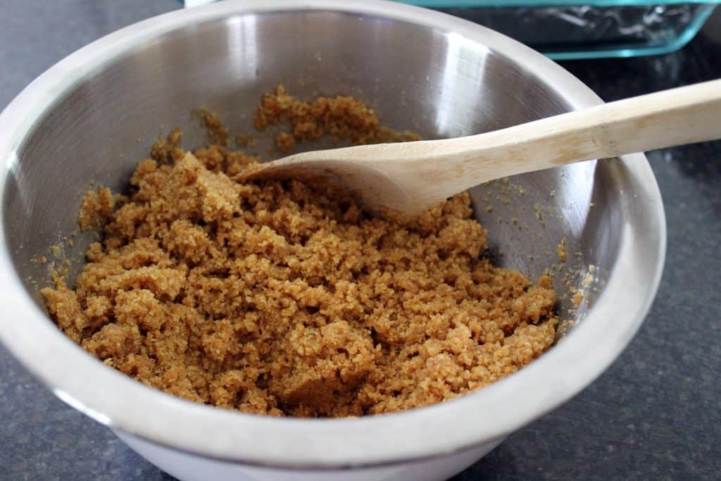 mixing bowl with grahams, sugar, and melted butter and wooden spoon