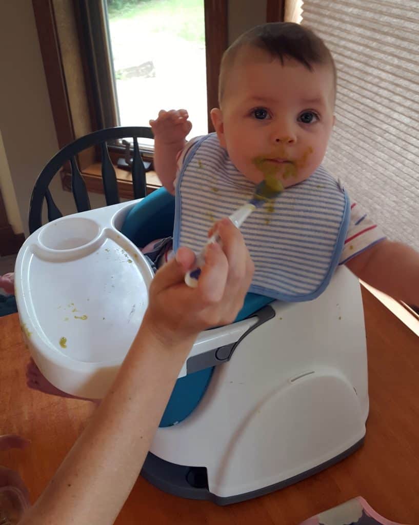 baby with green peas all over her face