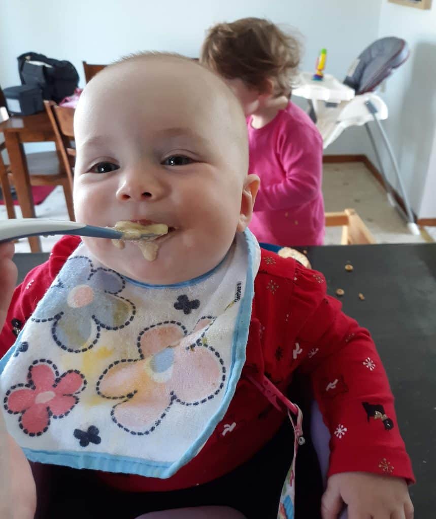 Happy baby with spoon of pureed baby food in mouth