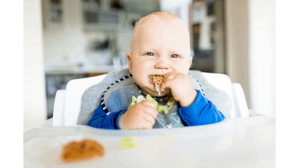 a baby in a high chair feeding himself