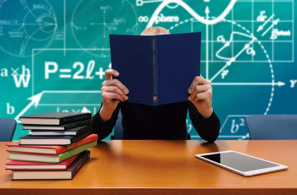 person sitting at desk in front of chalkboard reading