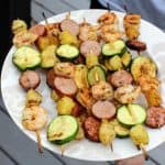plate full of shrimp, sausage, pineapple, and zucchini kabobs