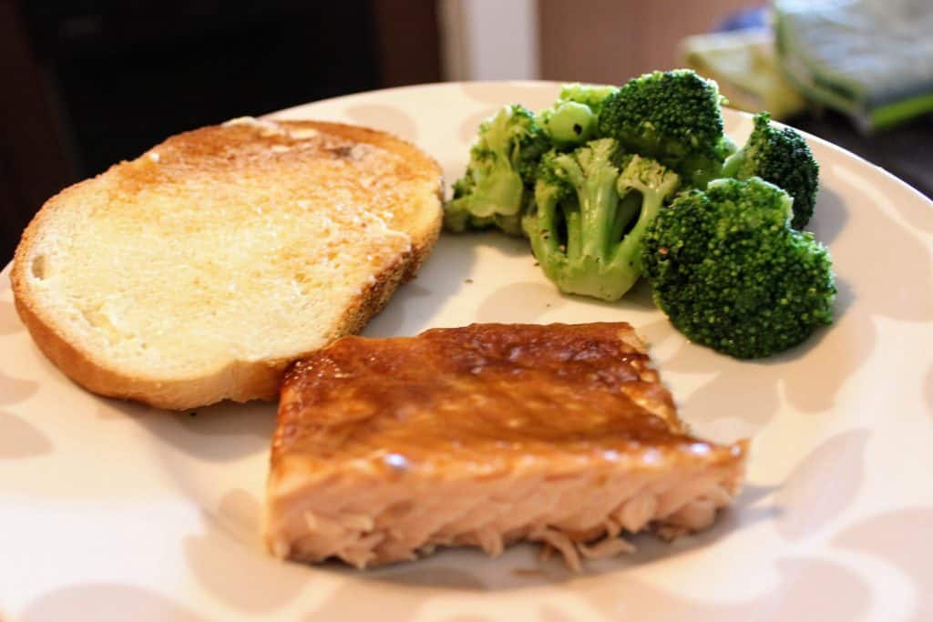 plate with a portion of salmon, a slice of buttered bread, and broccoli