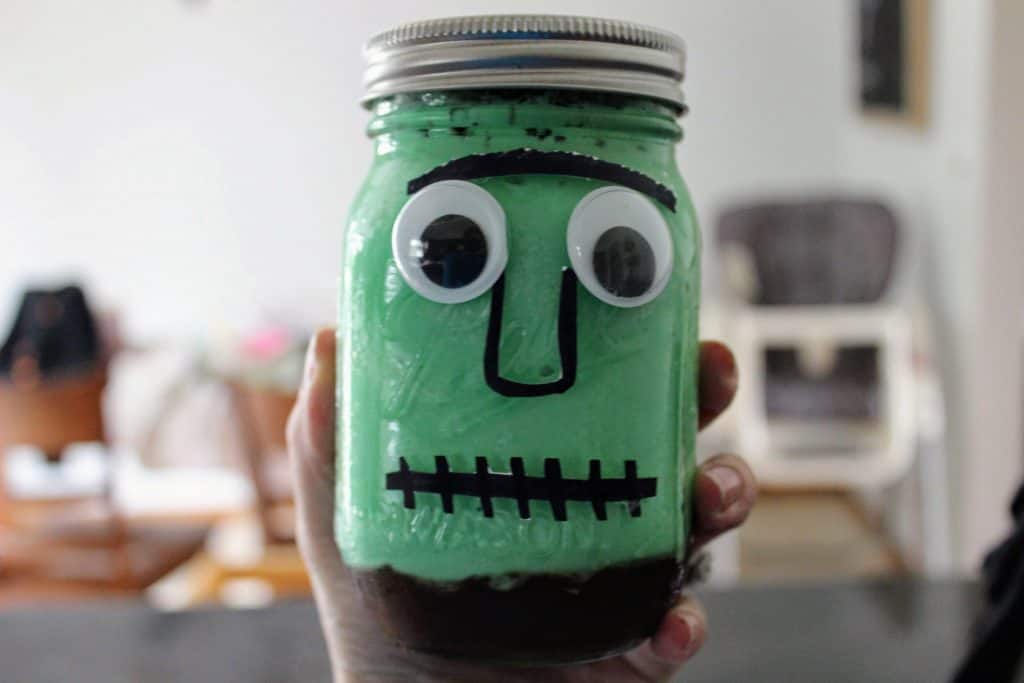 Green ice cream on top of fudge in a mason jar with Frankenstein's monster 's face glued on