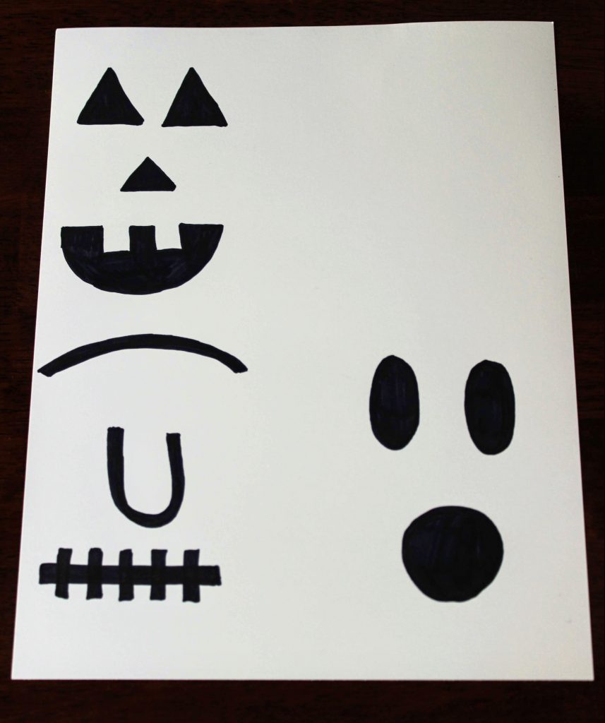 white sheet of cardstock with pumpkin, ghost, and Frankenstein's monster's facial features drawn on in black sharpie