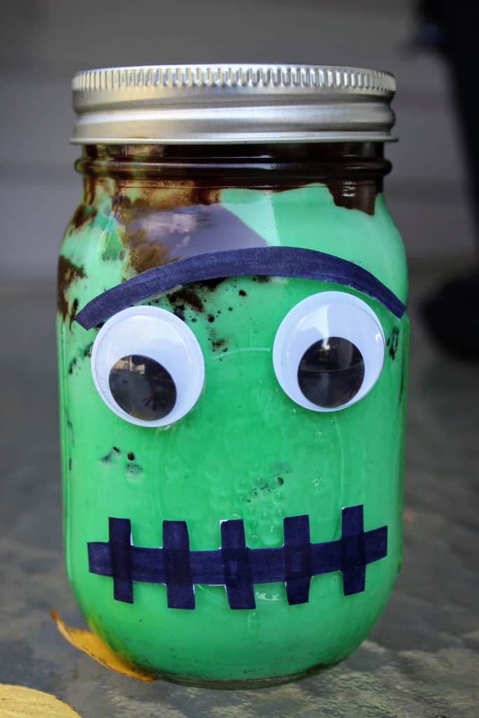 Green ice cream with fudge topping in a mason jar with paper and googly eyes to make it look like Frankenstein's monster