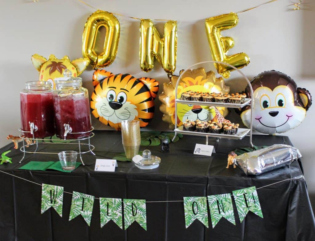 Wild One balloons and jungle animal balloons behind beverage and cake table