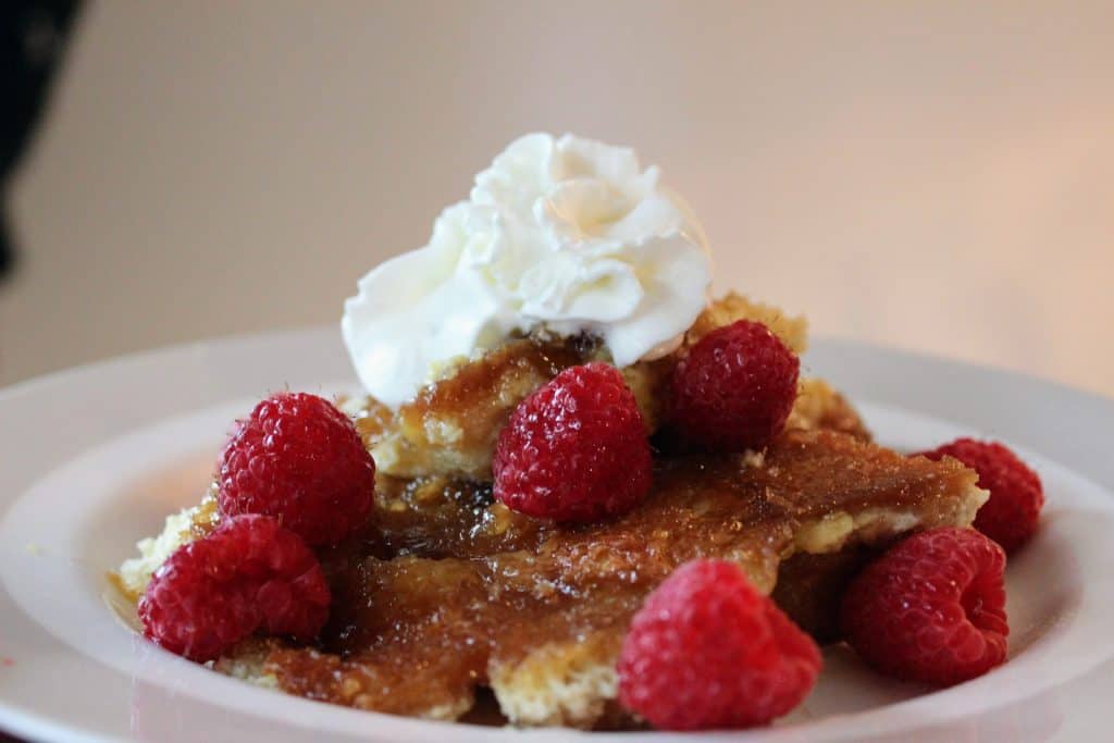 plate of creme brulee french toast topped with raspberries and whipped cream