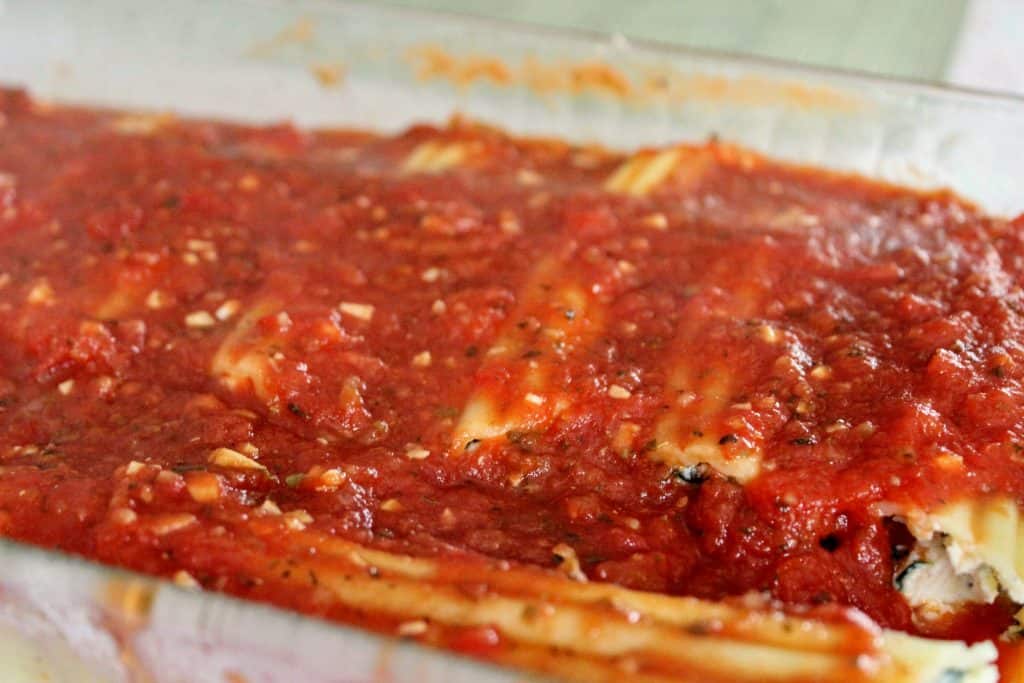 a cooked pan of stuffed manicotti shells with red sauce on top
