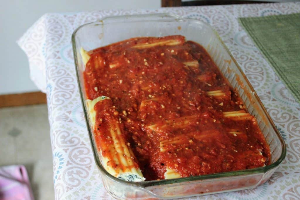 stuffed manicotti noodles in a 9x13 pan with red sauce poured on top