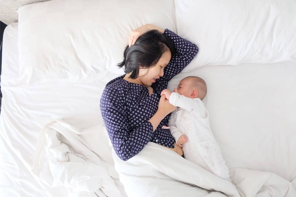 mom laying with baby on bed with white sheets