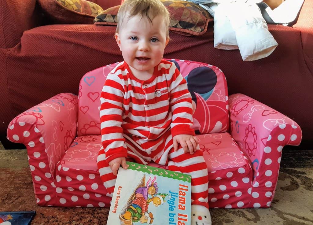 toddler sitting on child's couch with a book