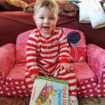 toddler sitting on child's couch with a book